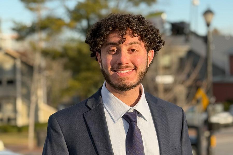 young man with beard, suit and tie in residential neighborhood smiling