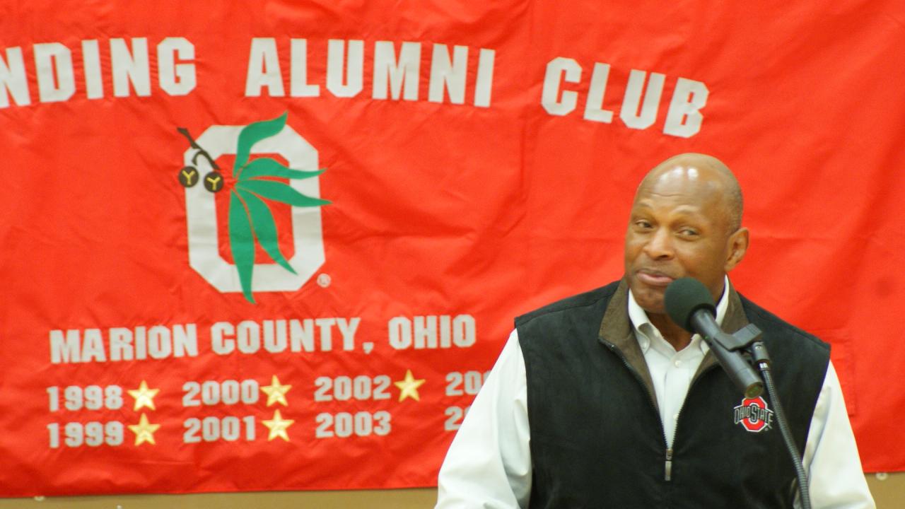 Man standing in front of red banner speaking at podium